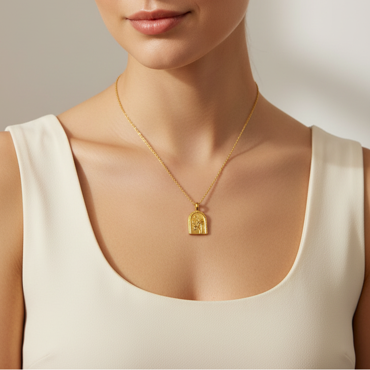 Gold necklace with a pendant worn by a person in a white top against a neutral background