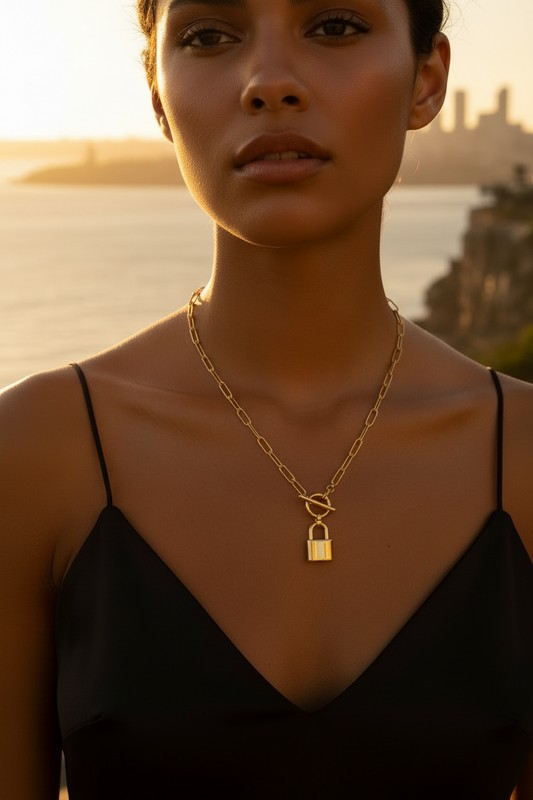 Woman wearing a gold necklace with a lock pendant against a sunset backdrop.