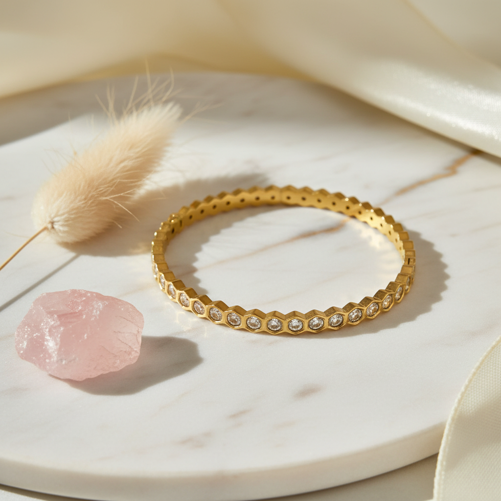 Gold bracelet with small stones on a white surface with a pink crystal and dried grass.