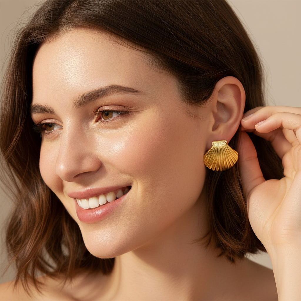 Gold shell earrings on a marble tray with natural shells on a beige background